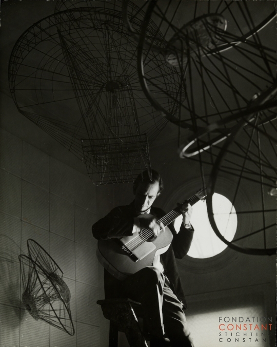 Constant Nieuwenhuys-Constant speelt gitaar op ladder, 1962