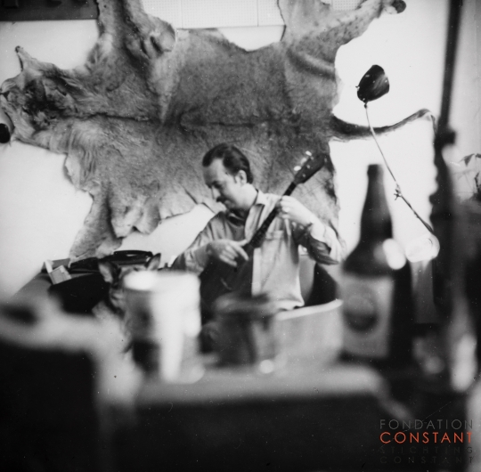 Constant plays guitar in front of lion skin, 1963